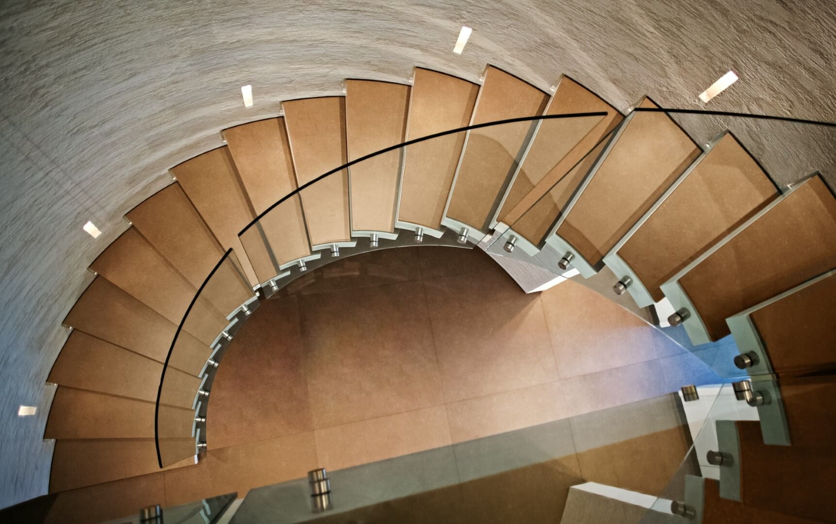 מבט מלמעלה על מדרגות לולייניות ספיראלה מקוריאן קופסא לבנה ומעל קוריאן בגוון שעורה ועץ סַנְדָל, ומעקה ספירלי מזכוכית אקסטרה קליר