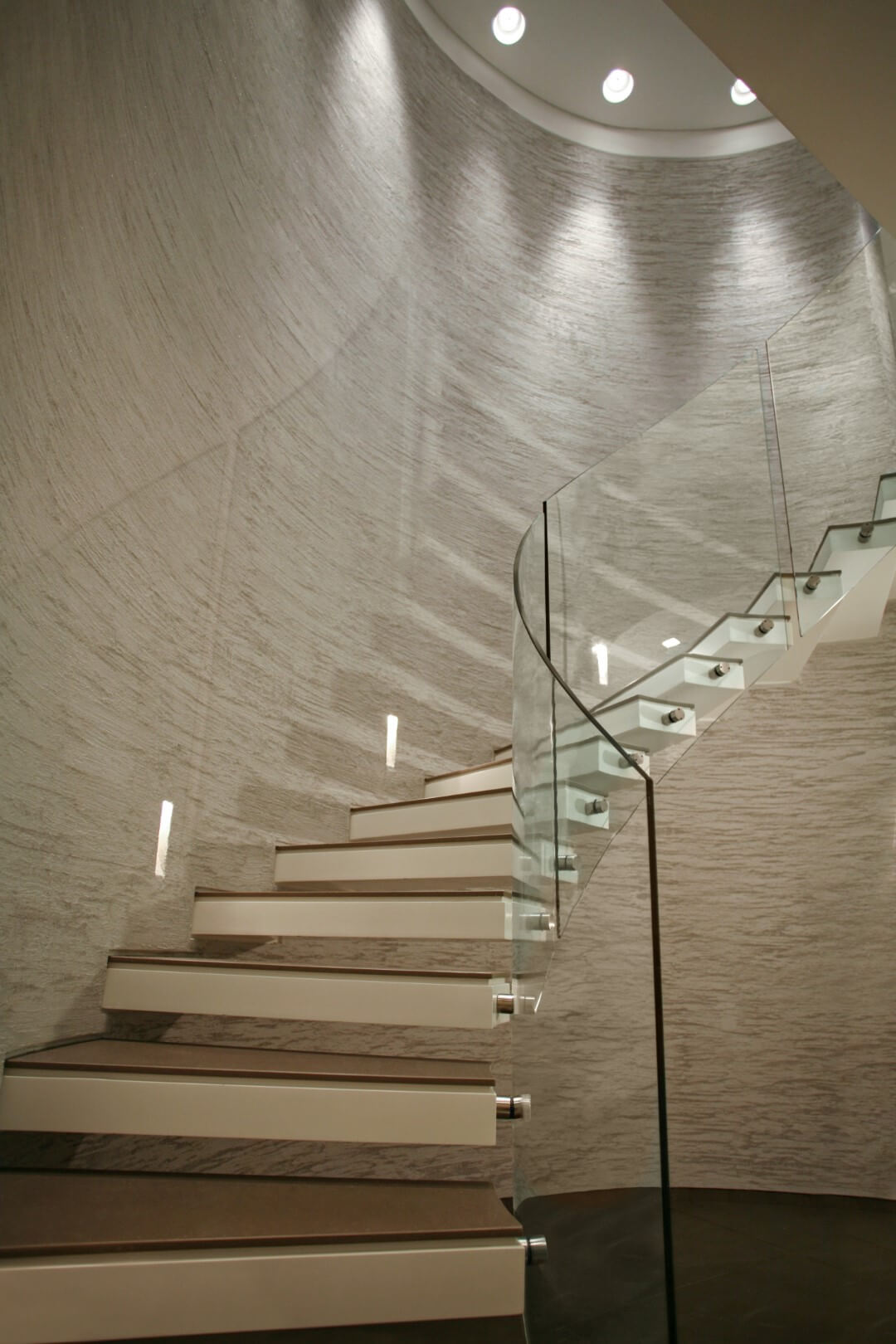 מדרגות ספירליות מקוריאן עם מעקה ספירלי מזכוכית עולות לקומה השניה לאורך הקיר