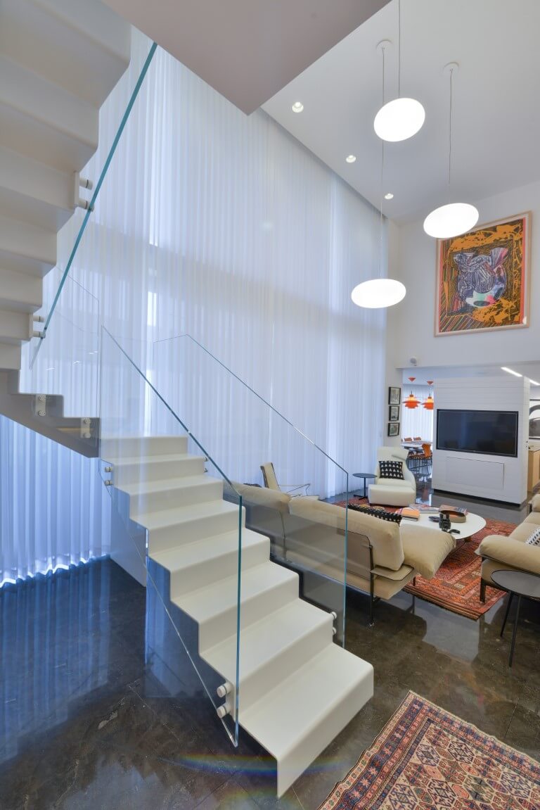 שלושה גרמי מדרגות מברזל לבן בליווי של מעקה זכוכית על רקע הסלון המעוצב