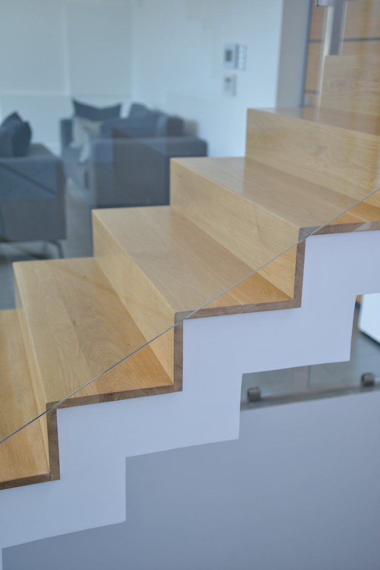 מדרגות עץ בהיר משולבות עם מעקה זכוכית וידיות עץ