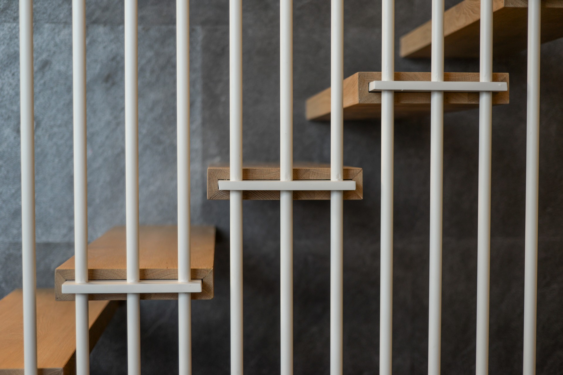 מדרגות ברזל לבן עטופות בעץ אלון משולבות במדרגות עץ מרחפות לצד מעקה ברזל לבן עם ידית מעץ ומעקות זכוכית