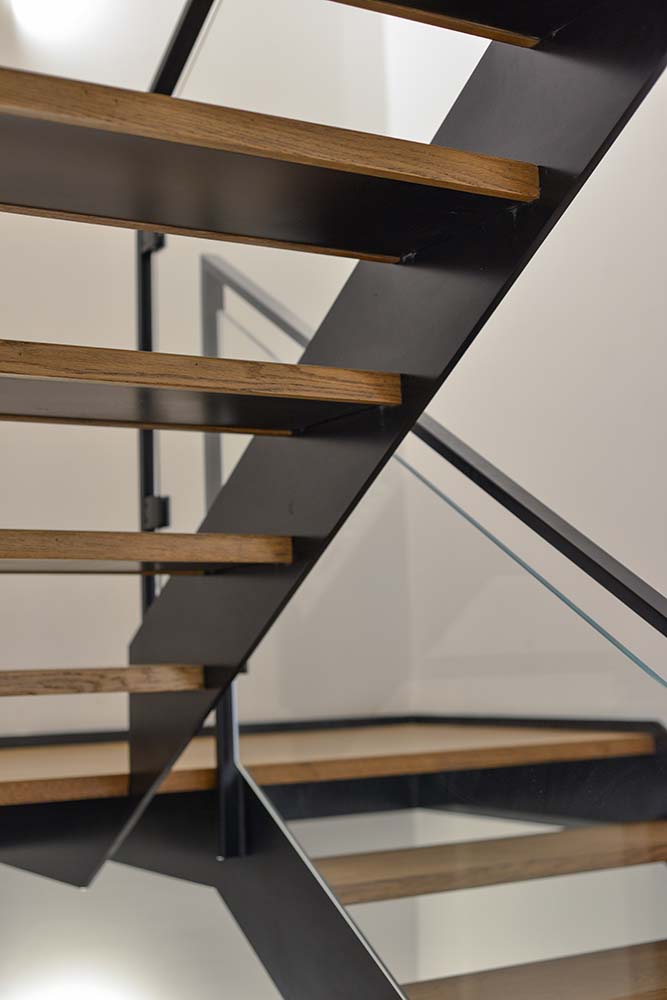 מבט מאחורה על שני גרמי מדרגות ברזל שחור עם שלבי עץ אלון יפייפה ומעקה ברזל שחור וזכוכית בוילה בתל אביב